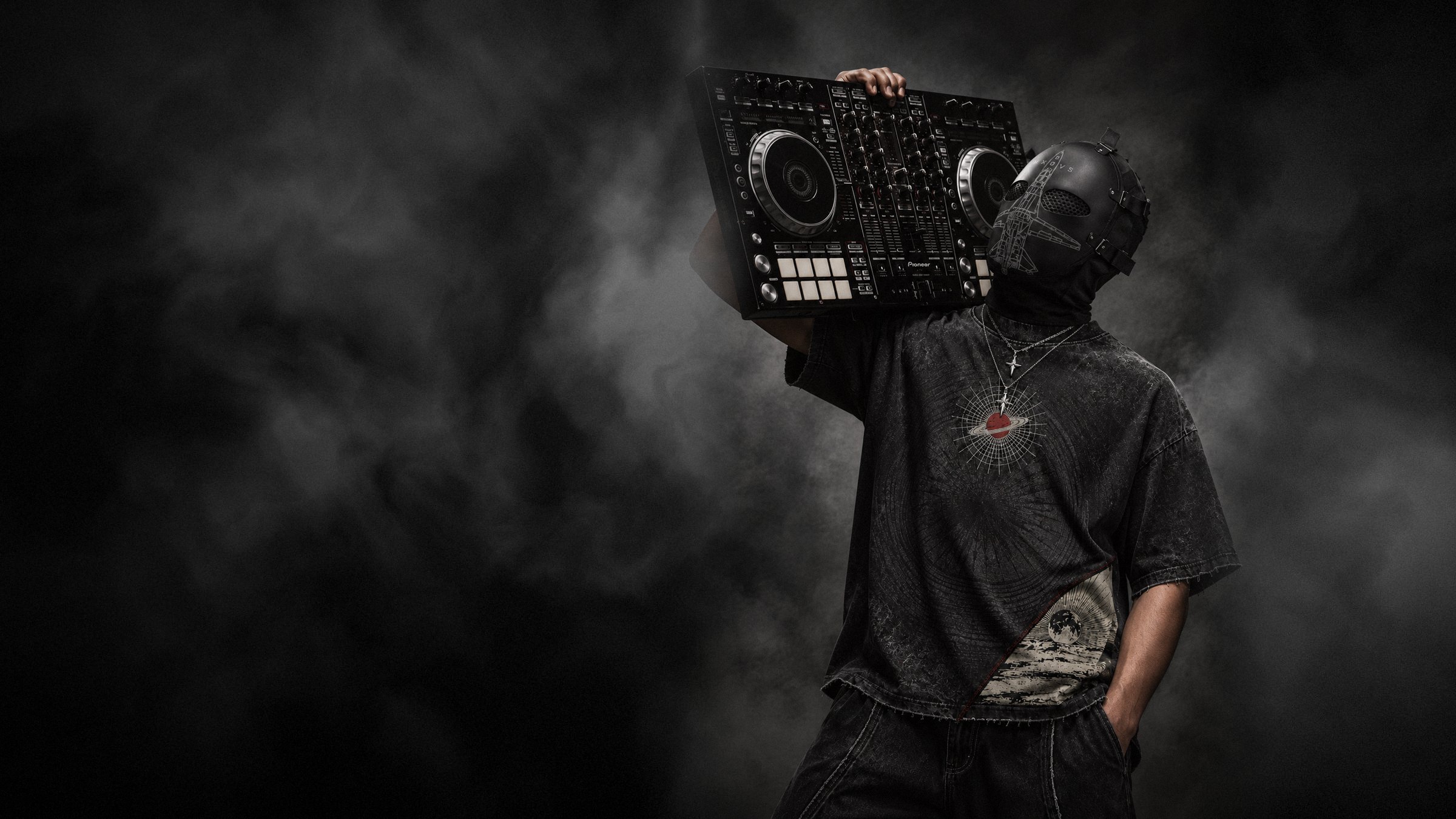 A masked figure in the MØSH Unresolved tee holding DJ decks on his shoulder in the smoke